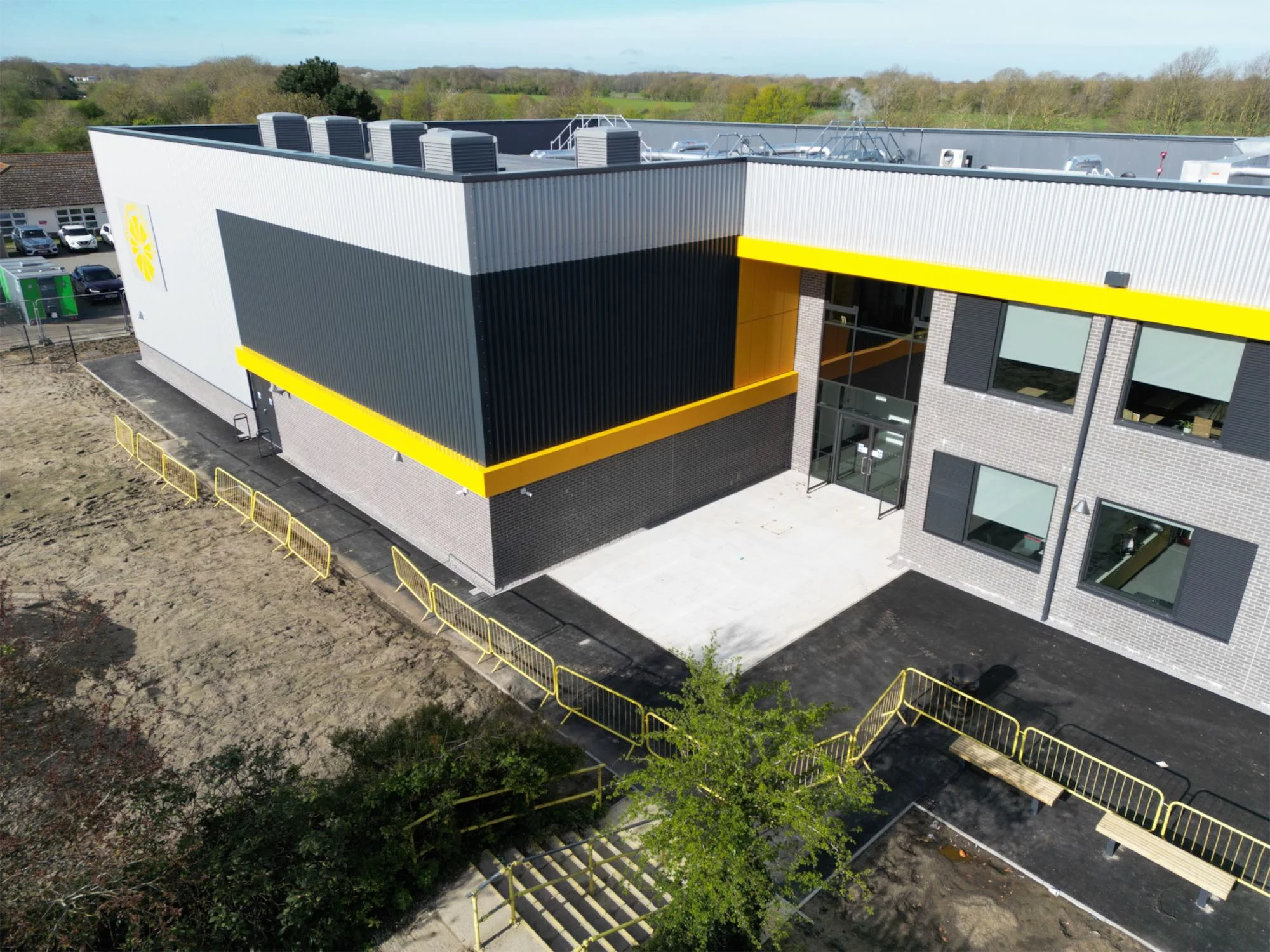 Aerial of the entrance corner: anthracite and silver cladding with the yellow canopy band