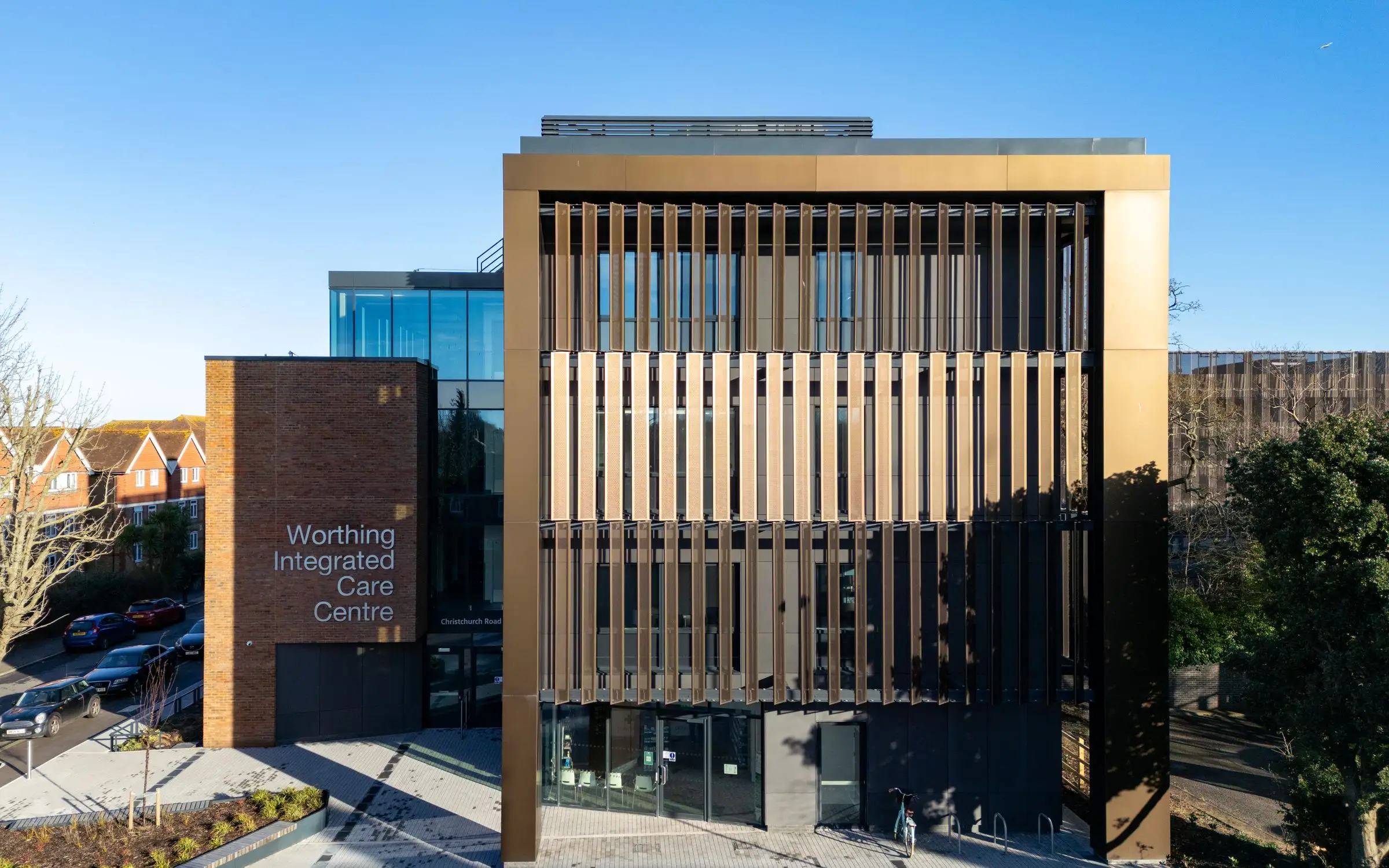 Front elevation of Worthing Integrated Care Centre: bronze aluminium panels framing the glazing, next to the brick name block